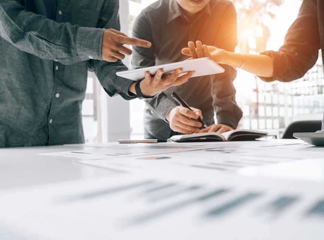 Three People Looking At Electronic Tablet Over A Desk 600X400