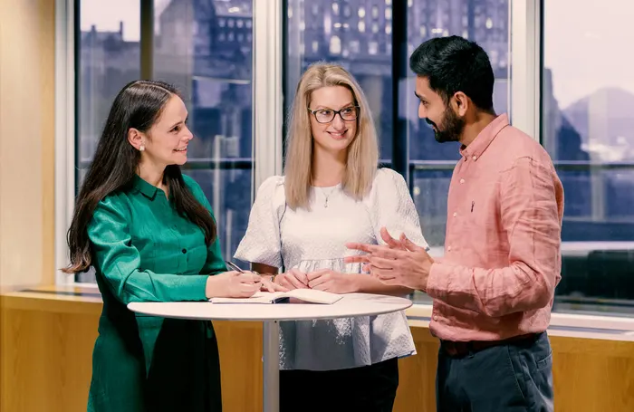 Three people standing at a table beside window