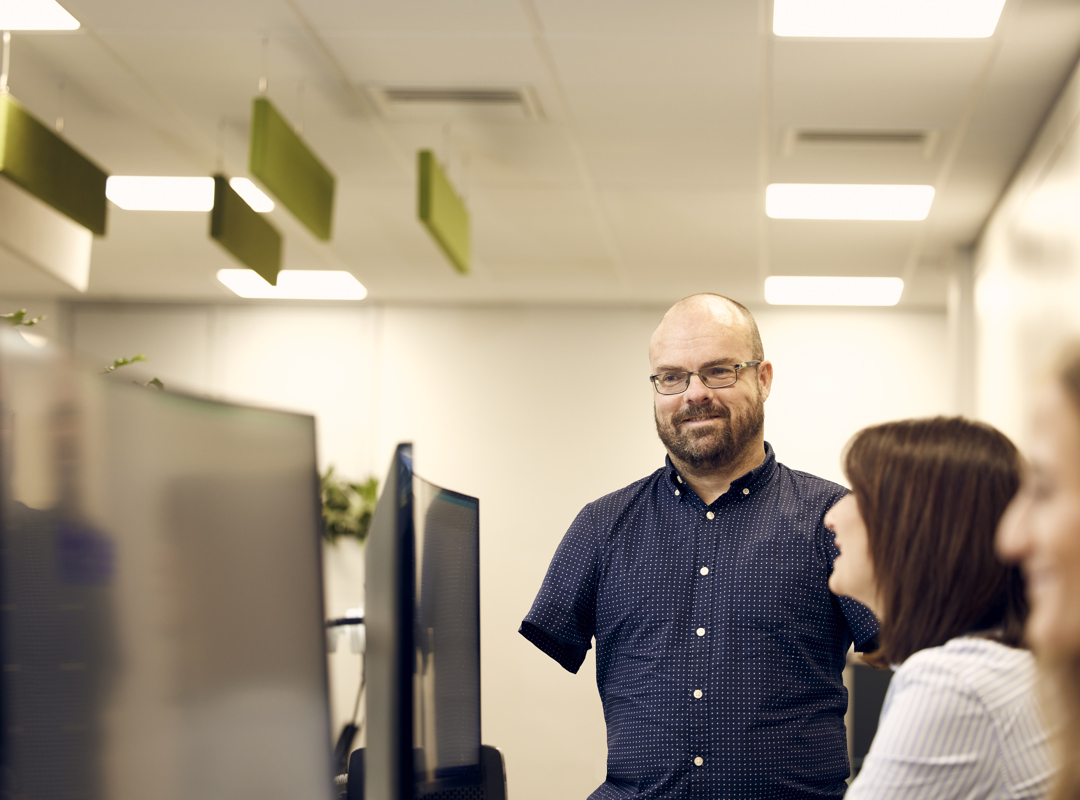 Man Talking To A Colleague At Their Desk